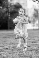 Young girl with a teddy bear running joyfully across a grassy field, wearing a light dress and sneakers, capturing the essence of childhood playfulness and freedom