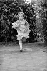 Young girl with a teddy bear running joyfully across a grassy field, wearing a light dress and sneakers, capturing the essence of childhood playfulness and freedom