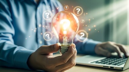 Person holding glowing lightbulb with question marks around it while typing on laptop