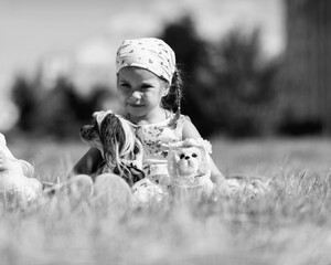 Young girl with braided hair wearing a patterned dress and headscarf is playing with toys on a grassy field, surrounded by colorful play items and a joyful atmosphere