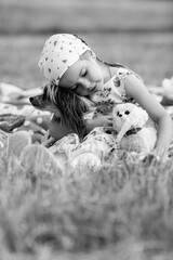 Young girl with braided hair wearing a patterned dress and headscarf is playing with toys on a grassy field, surrounded by colorful play items and a joyful atmosphere