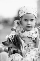 Young girl with braided hair wearing a patterned dress and headscarf is playing with toys on a grassy field, surrounded by colorful play items and a joyful atmosphere