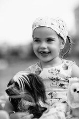 Young girl with braided hair wearing a patterned dress and headscarf is playing with toys on a grassy field, surrounded by colorful play items and a joyful atmosphere