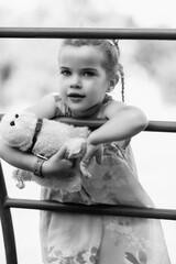 Young girl with braided hair wearing a patterned dress and headscarf is playing with toys on a grassy field, surrounded by colorful play items and a joyful atmosphere