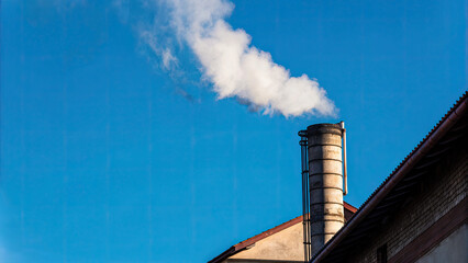 White smoke rises from the chimney concept. Smoke rising from a factory chimney against a clear blue sky.