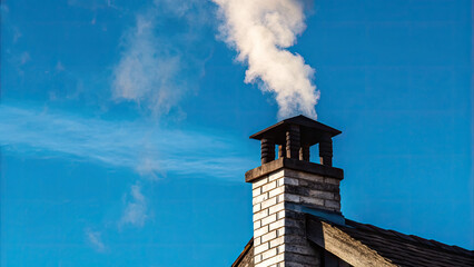 White smoke rises from the chimney concept. A chimney with smoke against a clear blue sky, evoking warmth.