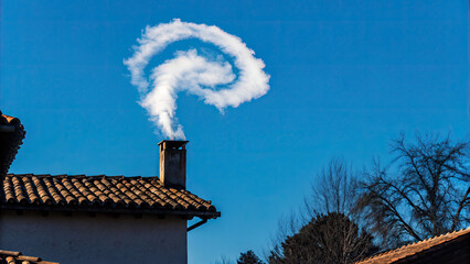 White smoke rises from the chimney concept. A spiral of smoke rises from a chimney against a clear blue sky.