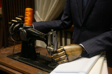 A person with a metallic prosthetic hand operates an antique sewing machine with vibrant orange...