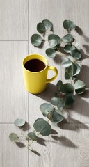Yellow mug of dark liquid rests near eucalyptus sprigs.