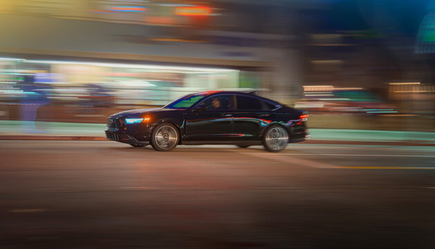 LOS ANGELES, CA - December 25, 2025: Black Honda Accord sedan car driving through dark street intersection at night. Blurred motion