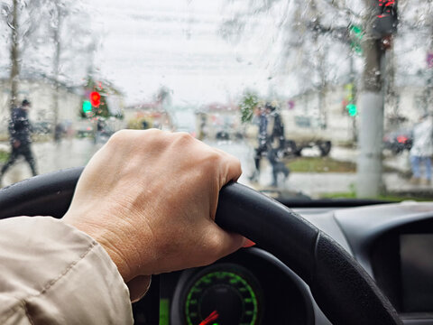 Driving through city streets in rain with wet windshield and urban traffic seen from the car's perspective