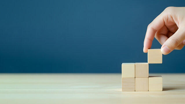 Hand placing a wooden block on top of stacked blocks