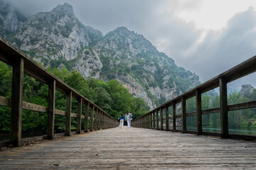 A wooden bridge with a view of mountains and a lake. The bridge is empty and the sky is cloudy