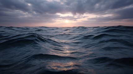 Dark choppy ocean waves reflecting the soft light of a dramatic sunrise under a moody overcast sky