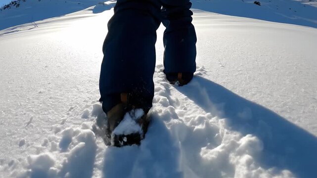 Low angle view of hiker legs trudging through deep powder snow in mountains. Scene conveys winter exploration and cold weather. Ideal for travel and outdoor adventure concepts.