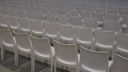 Empty white chairs arranged in rows inside an indoor event hall