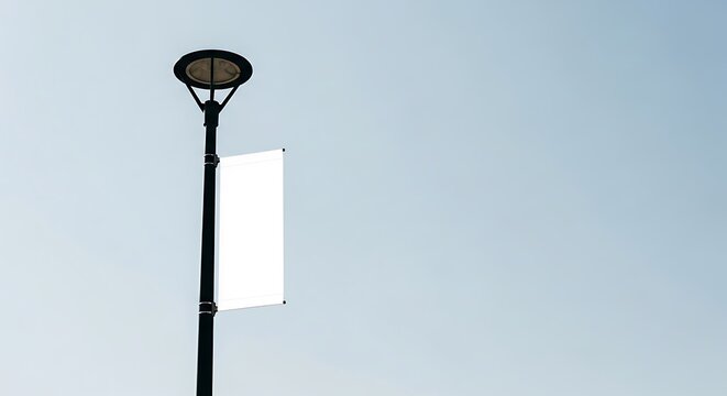 A tall black street light pole with a blank white vertical banner for advertising or public messaging against a clear light blue sky