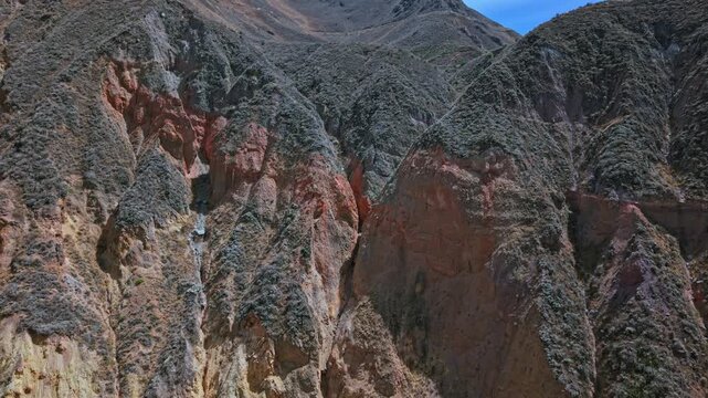 Forward-moving drone approaches striking red slice of layered sediment inside Colca Canyon, Peru. The vivid strata and eroded textures highlight ancient geological processes shaping the canyon walls.