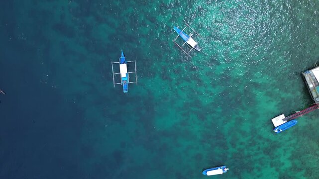 Top down aerial drone footage of several small boats floating in clear turquoise tropical water at Sabang Bay in Puerto Galera, Philippines, creating a calm marine pattern ideal for travel and nature.