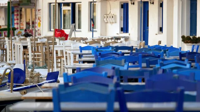 Charming view of a traditional empty Greek restaurant at sunrise in Elafonisos. Iconic blue chairs and a peaceful atmosphere capture the authentic Mediterranean morning light.