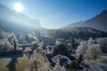 Picturesque, wintry Aschau im Chiemgau, Bavaria. Trees and roofs are covered with a thick layer of frost, surrounded by snow-capped mountains in the bright winter sun.