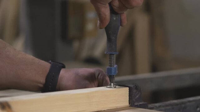 Detailed Scene Capturing Worker Securing Wooden Panel With Screwdriver In Warm Illuminated Workshop. Media