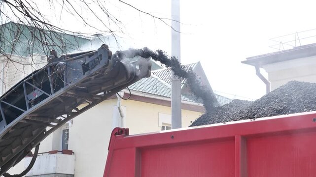 Asphalt milling machine loading recycled material into a dump truck, road resurfacing