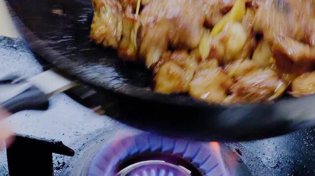 A close-up of a chef stir-frying pork ribs