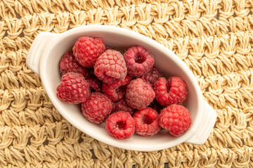 Red ripe raspberries isolated on a straw mat, top view, macro.