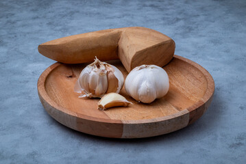 Fresh garlic is placed in a mortar and pestle on a marble-patterned wooden table.