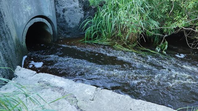 Dark water discharging from concrete culvert pipe, polluting natural stream