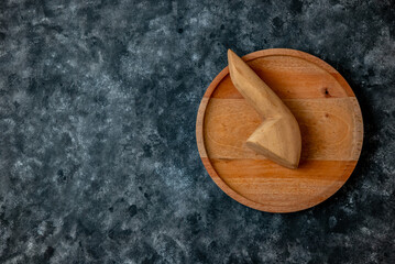 Top view of a round wooden plate with wooden tools on a dark textured background. Minimalist concept with ample copy space.