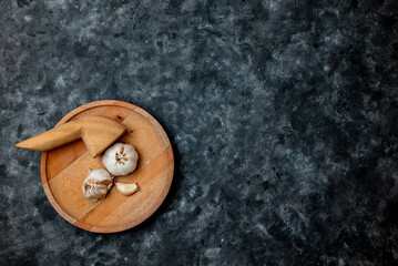Fresh garlic is placed on a wooden mortar and pestle against a dark background.