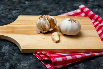 Fresh garlic is placed on a wooden cutting board with a red and white checkered cloth