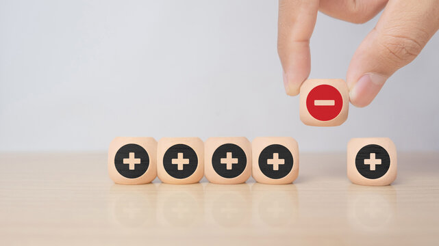 Hand removing a minus symbol from a row of plus icons on wooden blocks, symbolizing problem solving, correction, decision making, and eliminating negative factors.