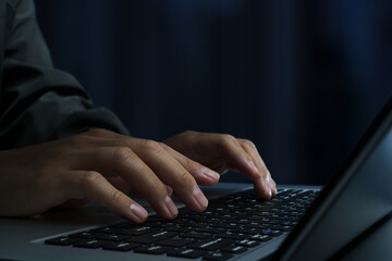 Hacker using laptop computer at desk in dark room. Closeup of hands and keyboard. Cyber crime image.
