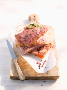 Sliced pork in aspic with pepper on wood board and knife in studio