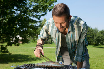 Mid adult using tongs to grill food in an outdoor park setting