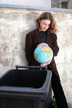 Teenage girl holding globe near litter bin showing environmental concern
