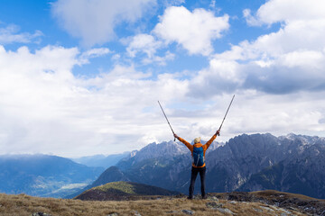 Hiker on mountain summit with walking sticks celebrating success