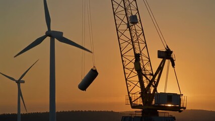 Heavy-duty crane precisely positioning a wind turbine component at sunset, symbolizing the significant progress in sustainable energy infrastructure and a commitment to a greener future