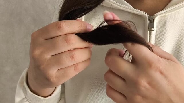 Young brunette woman winding thin ends of hair on her finger. The girl touches the dry ends of her hair. The concept of hair loss.