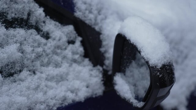 A close-up of a car mirror covered in snow on a snowy winter day. Snowfall.
