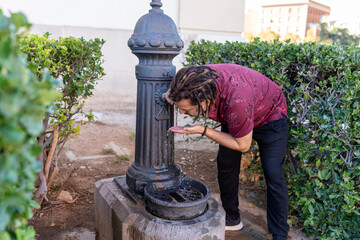 Man with dreadlocks drinking water from a traditional public fountain in the city