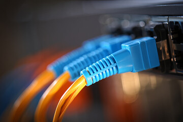 A close-up macro of blue fiber optic and Ethernet RJ45 cables with connectors on a tabl,e providing a high-speed digital data connection for computer network technology and internet equipment