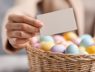 Woman holding blank card over a basket full of colorful pastel Easter eggs. Perfect for spring holidays, greetings, or promotional messages.
