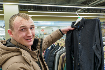 A smiling man chooses a shirt in the supermarket. Clothing stores. Textile industry. Buyer