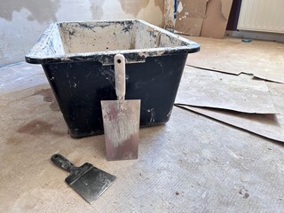 Paint tray with wall putty and plastering tools on the floor during wall finishing, illustrating the interior renovation and construction process