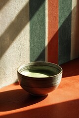 Close-up view of a ceramic bowl filled with green liquid. Striped wall and red surface