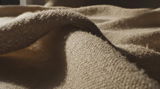 Soft beige linen fabric texture draped over surface with visible woven natural fiber thread and soft folds, warm neutral woven textile cloth drape conveying calm organic cozy comfort and soft fabric